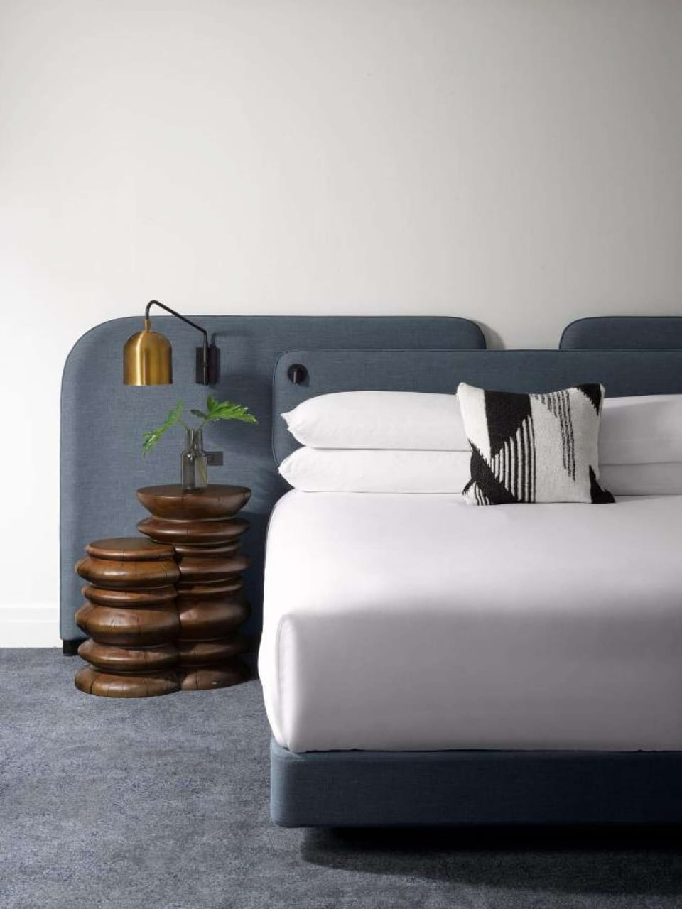 Modern bed with stacked wood nightstand and brass wall lamp