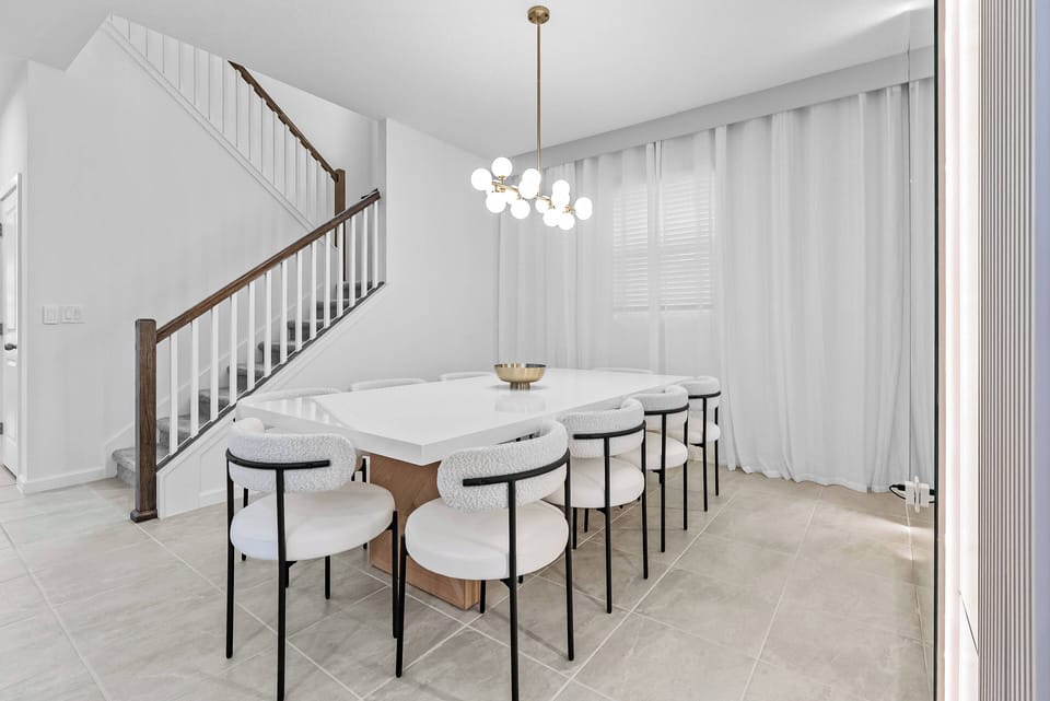 Bright and airy, this dining area features a sleek white table surrounded by stylish chairs, perfect for family meals. The warm wood accents from the staircase and the soft glow of the pendant light create a welcoming ambiance.