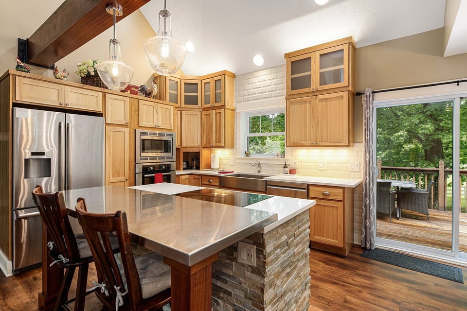 Large kitchen island w/ stone base, wood cabinetry & warm overhead lighting.