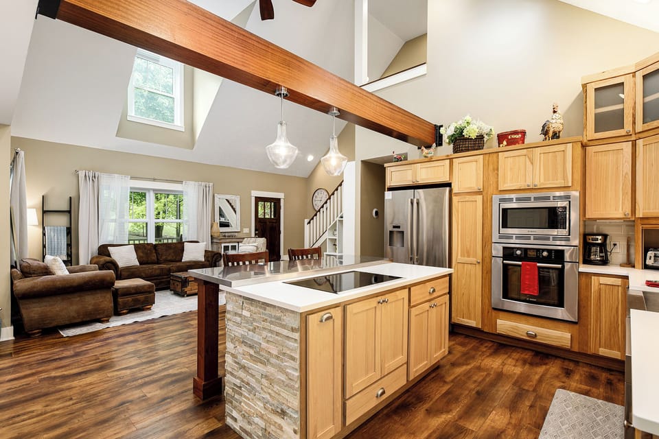 Open-concept kitchen flowing into the living area beneath vaulted ceilings & exposed beams.