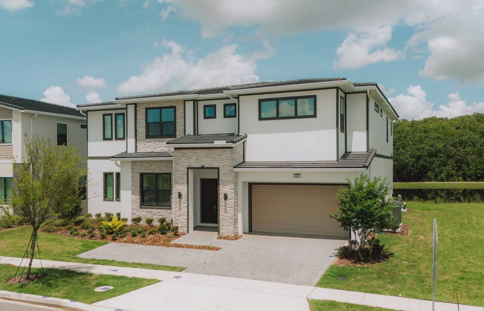 Experience a stunning exterior with bright white walls and large windows that fill the space with natural light. The lush landscaping and well-kept driveway offer an inviting first impression for your stay.
