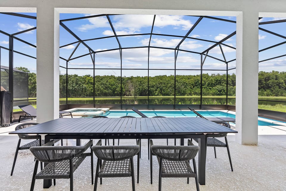 Enjoy al fresco dining at a sleek table with stylish black chairs, overlooking a crystal-clear pool. The spacious screened enclosure offers seamless views of the lush greenery, perfect for your relaxation and enjoyment.