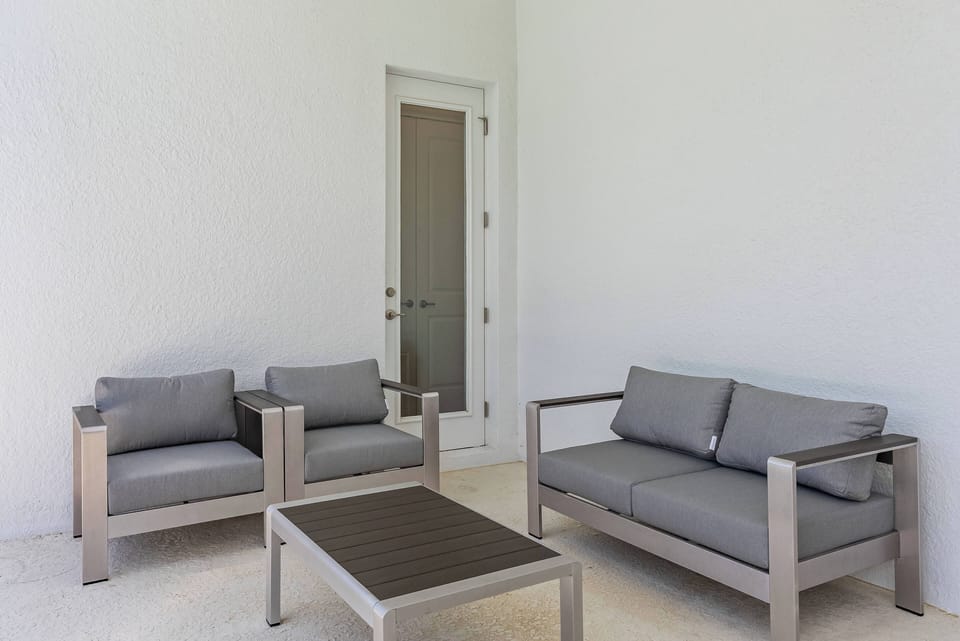 Enjoy our serene outdoor lounge with sleek gray seating and a chic coffee table, ideal for relaxation. Bright walls and plenty of natural light foster an inviting space for both casual chats and peaceful moments.