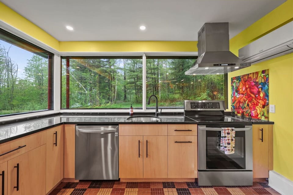 Alternate kitchen angle displaying the cooktop, built-in oven, range hood, and ample counter space with abundant natural light from surrounding windows.