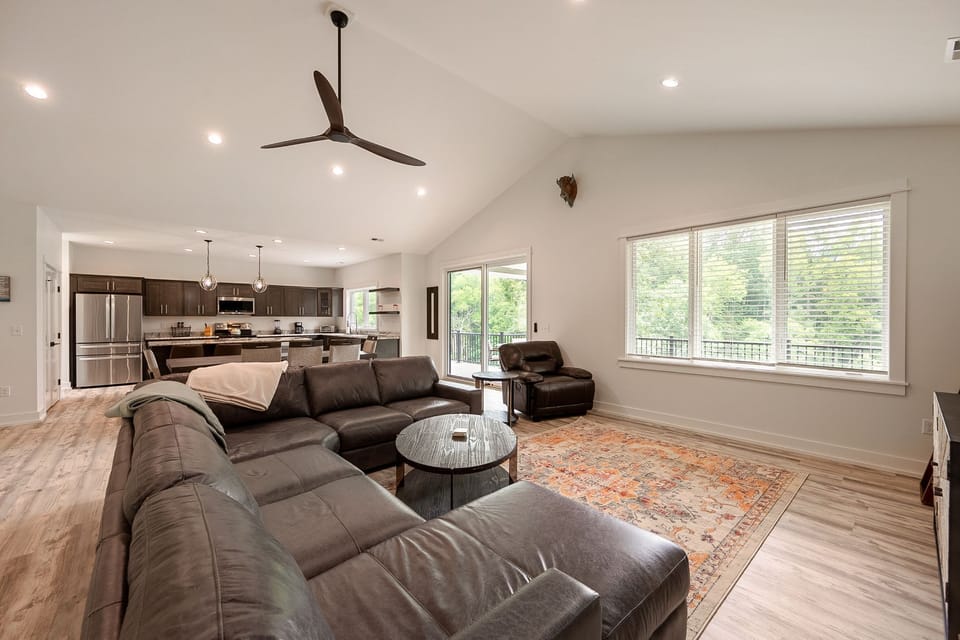 Open living area with leather sectional sofa, large windows, and natural light—ideal for gathering or watching TV.