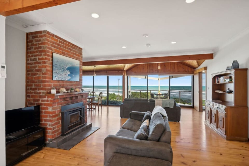 Let the day slow down in the living room, where timber floors, a fireplace, and sea views set an easy rhythm.