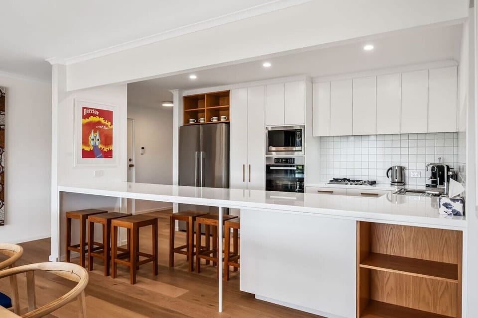 The well-equipped kitchen offers a long island and timber stools, creating an inviting spot for casual meals, morning coffee, and easy conversation while cooking.