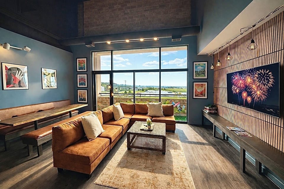 Spacious loft living room with a cozy sectional, floor-to-ceiling windows, and balcony views toward Lake Erie. Relax with a movie, watch fireworks on the big screen, or enjoy the natural light that fills this modern open space.