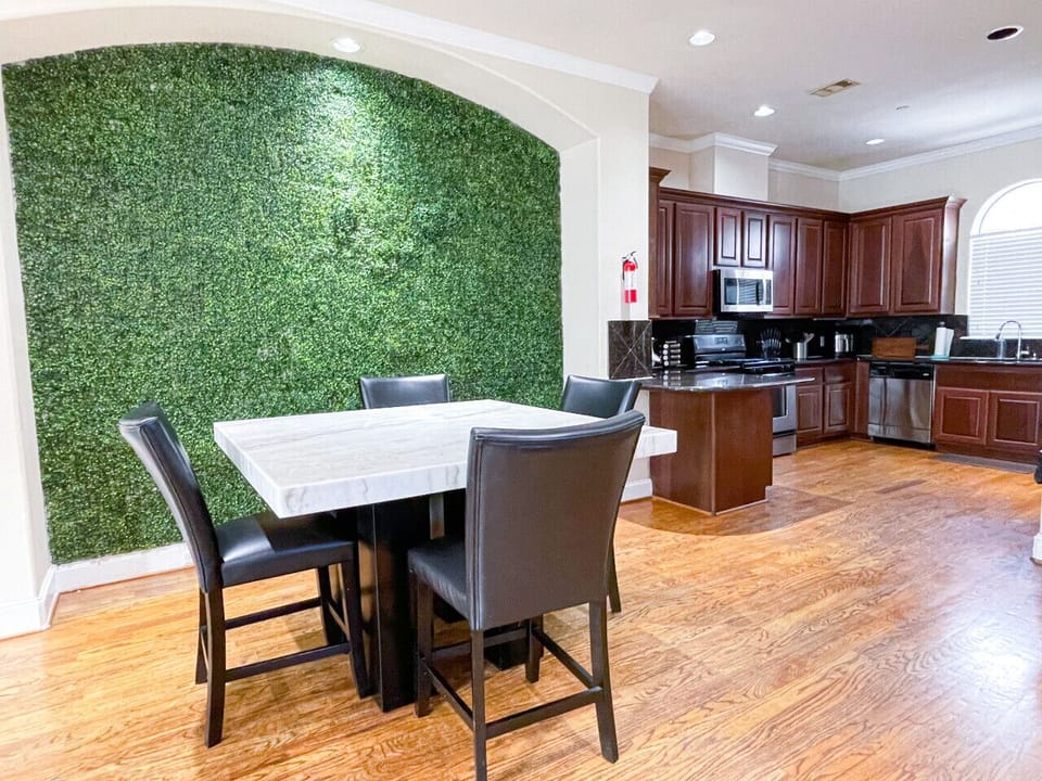 Gather around the modern marble dining table, framed by a chic grass wall backdrop, ideal for shared meals and picture-perfect moments.