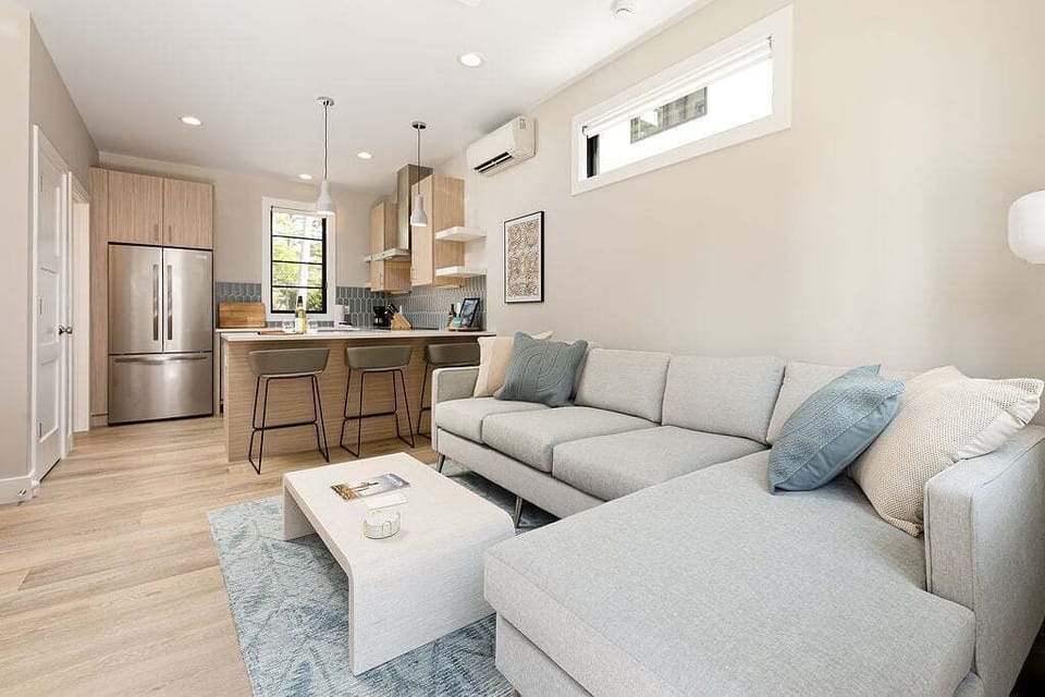 The living room features a large smart TV mounted above a stylish media console, a soft sectional sofa, and a chic coffee table. With warm wood floors and plenty of natural light, it's a perfect spot to relax and recharge.