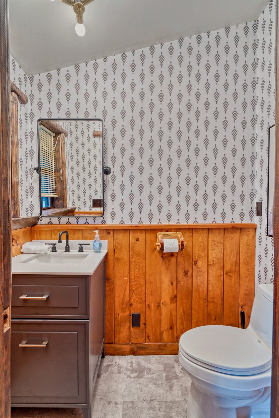 Bathroom with a sink vanity, toilet and patterned wallpaper.