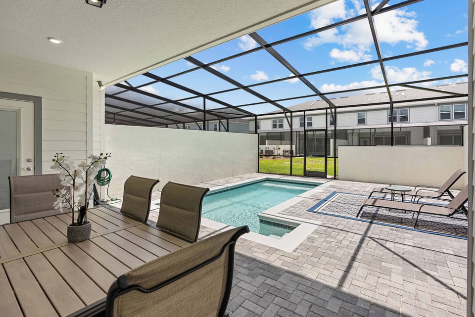 Step into your private oasis with a sparkling pool and a sunlit patio. Savor al fresco dining at the stylish wooden table, perfect for your group, all set against a backdrop of vibrant blue skies and lush greenery.