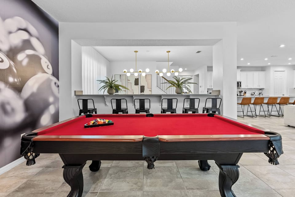 Join us at the stunning red billiards table for friendly competitions in a vibrant atmosphere. The sleek black frame and elegant pendant lights above create the perfect setting for relaxation and enjoyable moments with friends.