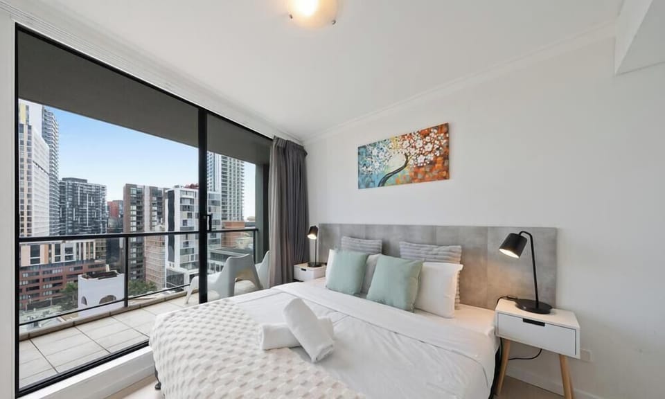 the bedroom showcasing how the large bed sits right next to expansive windows overlooking the urban skyline.