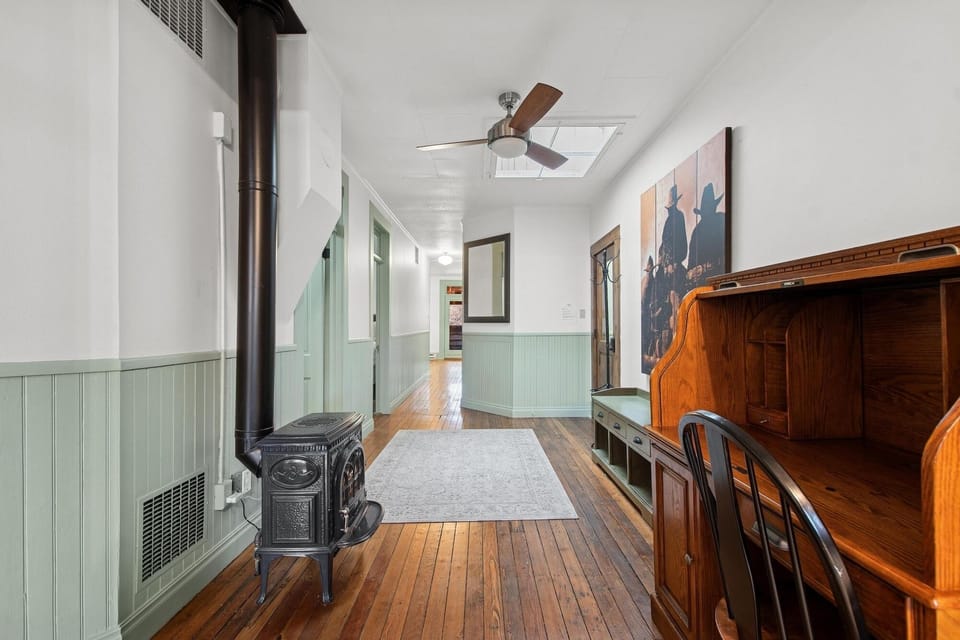 Step into this charming hallway where vintage wood stove warmth meets classic wainscoting and gleaming hardwood floors beneath your feet.