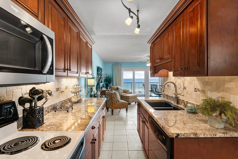 Long kitchen w/ granite counters, dark wood cabinets, & ocean views peeking through the window.