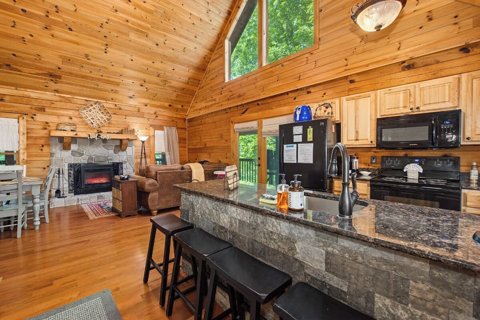 Gather around this spacious kitchen with gleaming countertops, modern appliances, and breakfast bar seating—perfect for preparing meals while enjoying the warm cabin ambiance and lush forest views through soaring windows.