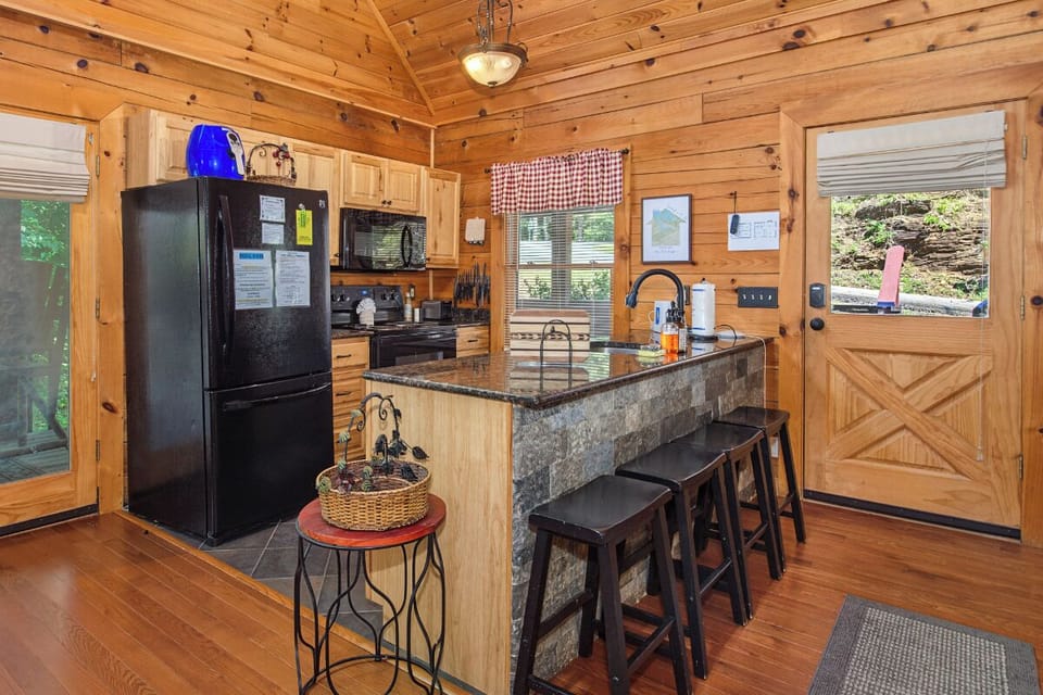 Your fully equipped kitchen blends rustic charm with modern convenience, featuring a spacious granite island perfect for morning coffee or meal prep in this cozy wood-paneled retreat.