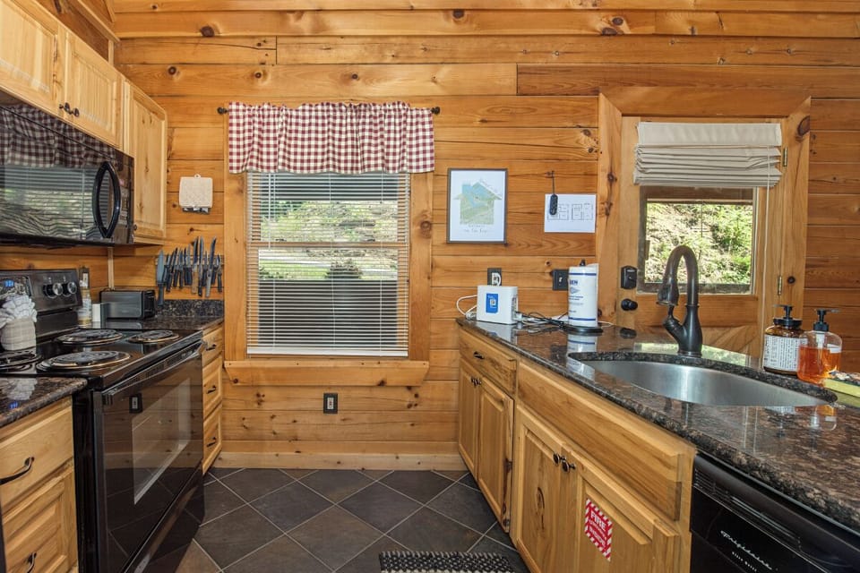 Your fully equipped cabin kitchen features warm wood tones, granite countertops, and modern appliances—perfect for preparing meals while enjoying scenic views through the windows.