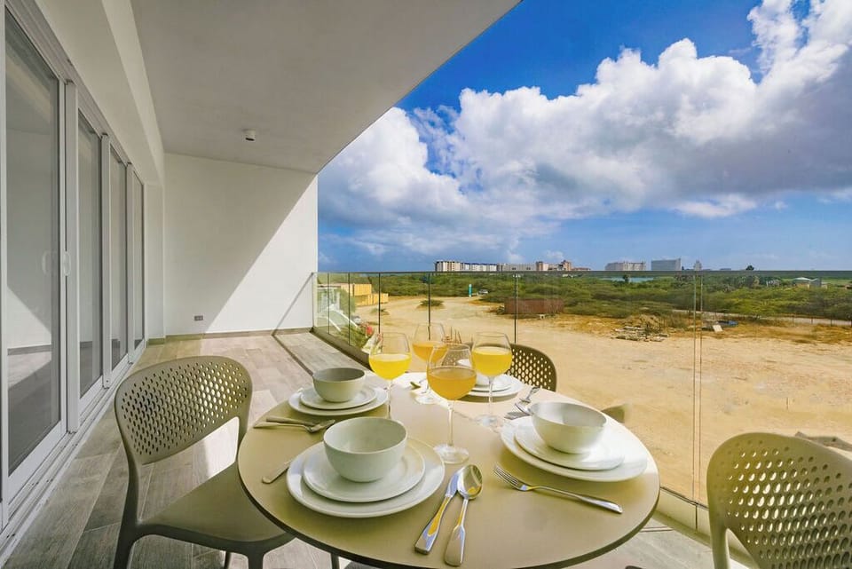 Enjoy morning juice on your private balcony as you take in sweeping coastal views, where fresh sea breezes and blue skies frame distant city buildings beyond open landscape.