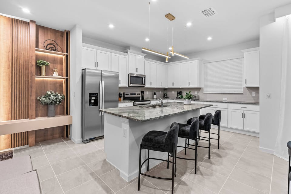 Welcome to this stylish kitchen, featuring sleek white cabinetry, rich wood accents, and polished stone countertops. The spacious island invites casual dining, all enhanced by contemporary lighting that adds warmth to the space.