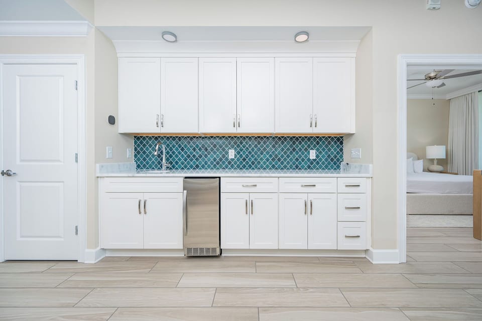 Prepare drinks at the wet bar with a vibrant backsplash, stainless appliances, and sleek cabintery