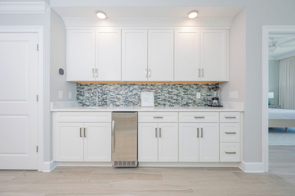 Prepare snacks and drinks at the wet bar featuring sleek cabinetry and a decorative backsplash