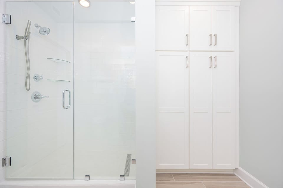 Spacious glass walk-in shower with modern fixtures, complemented by ample storage nearby