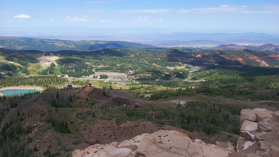 Aerial view showcasing the property's stunning mountain location, surrounded by expansive forests, rolling hills, and distant peaks under a clear blue sky.