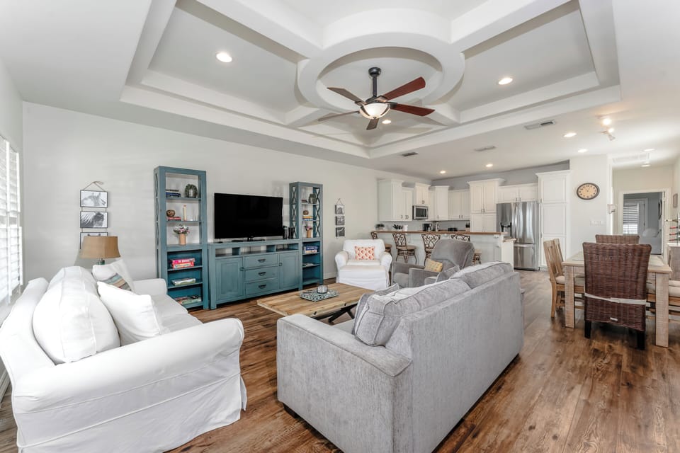 Bright and inviting living room featuring tray ceilings, coastal décor, and plenty of comfortable seating for the whole group