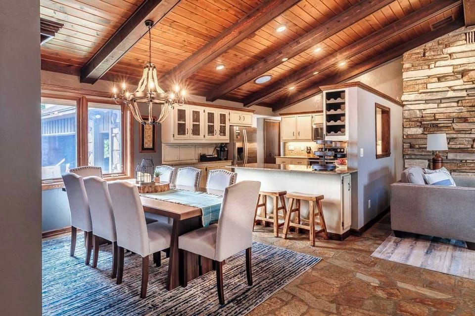 This view of the dining table highlights its connection to the fully stocked kitchen, complete with stainless steel appliances and a spacious island. Three counter stools offer additional seating for casual meals or keeping the cook company.