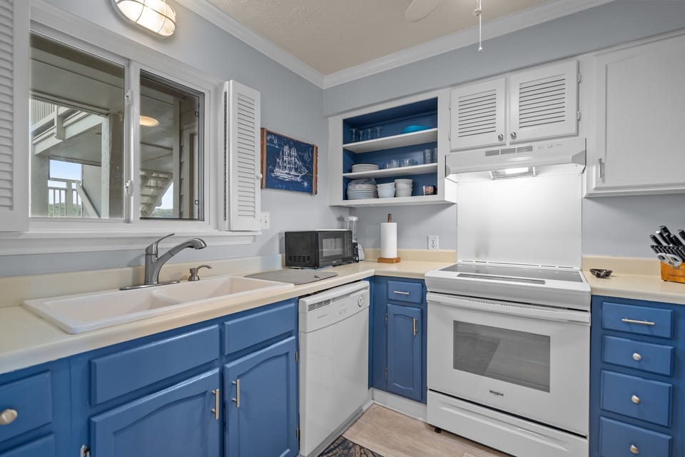 Oak Island, NC kitchen with blue lower cabinets, white appliances, stove, sink, dishwasher, microwave, coffee maker, ceiling fan, and nautical décor.