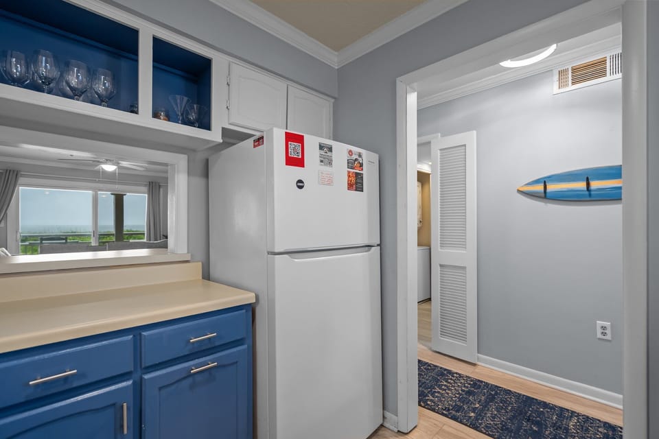Oak Island, NC kitchen with blue lower cabinets, white appliances, stove, sink, dishwasher, microwave, coffee maker, ceiling fan, and nautical décor.