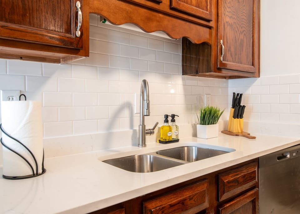 Bright and clean kitchen sink area with modern backsplash and essential utensils.