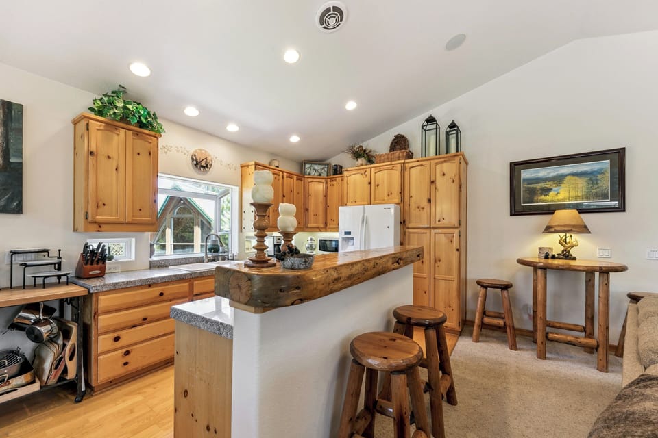 Gather around the warm wooden breakfast bar where rustic charm meets modern convenience in your mountain getaway kitchen.