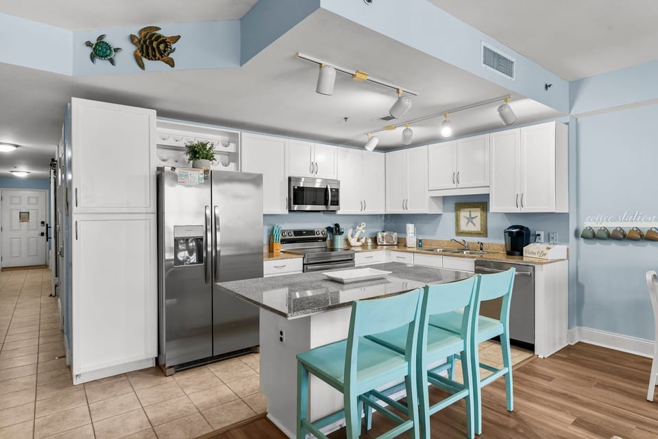 Modern kitchen with stainless steel appliances and a breakfast bar with turquoise chairs.