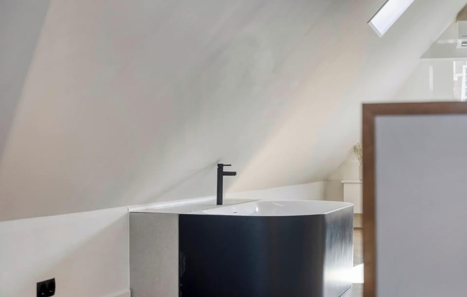 Statement bath in matte black with sloped ceiling light — design meets functionality.