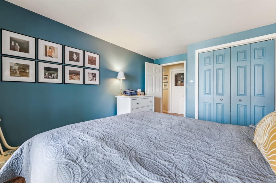 A warm and welcoming bedroom that invites you to settle in, featuring classic cottage decor, family photo gallery wall, and soft, layered linens.