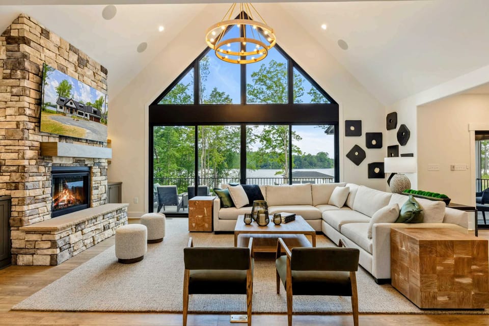 Great Room - A soaring, design-forward space where comfort meets lakefront beauty, anchored by a stone fireplace and gold chandelier.