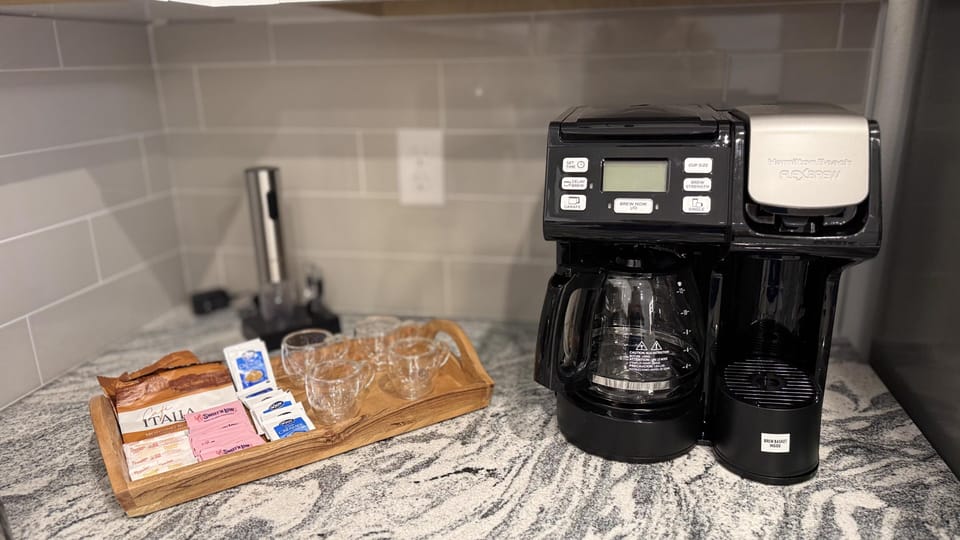 Modern kitchen station with a coffee maker and an assortment of teas and sugars.