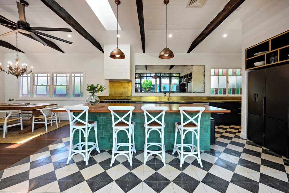 Expansive open-plan kitchen and dining space with bold checkered floors, timber island and elegant lighting — designed for connection and shared moments.