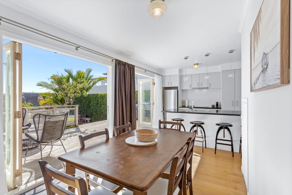 Dining area with a wooden table for six, opening to a sunny deck and modern kitchen.