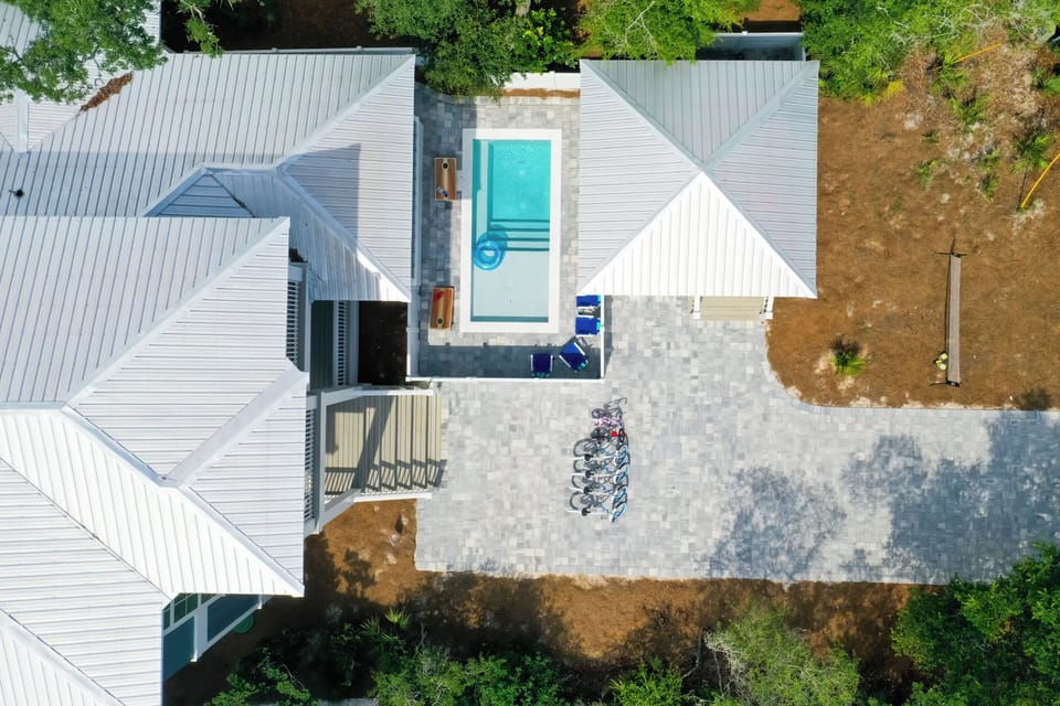 Aerial view of a modern vacation rental featuring a pristine swimming pool, spacious patio, and bikes ready for exploring the area.