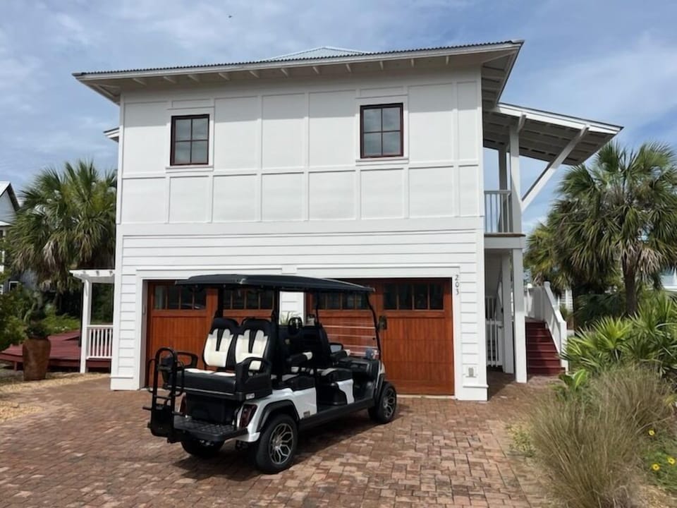 Modern two-story coastal home with convenient golf cart parking and tropical landscaping in a peaceful residential setting.