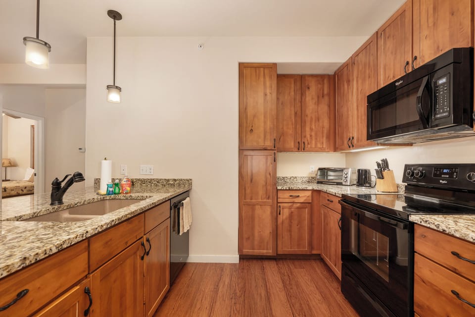 Your fully equipped kitchen at Ten Mile G-201 features warm wood cabinets, granite counters, and modern appliances for preparing memorable meals together.