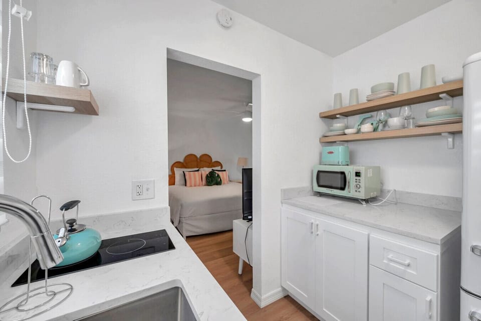 Kitchenette view w/ open shelving, compact appliances & clean, bright finishes.