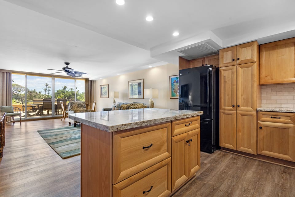 Your open-concept living space flows seamlessly from the granite-topped kitchen island to a sun-filled lounge and inviting balcony with warm tropical breezes and lush greenery just beyond.