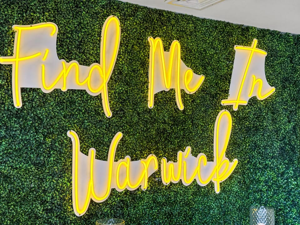 Instagrammable Touch: Bright neon sign invites fun in a lush green backdrop!