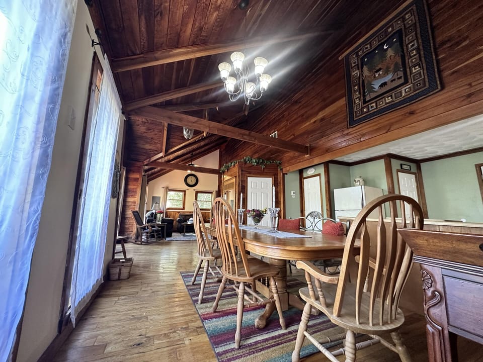 Wood-paneled vaulted ceiling and exposed beams frame the dining area with a wooden table and spindle-back chairs.