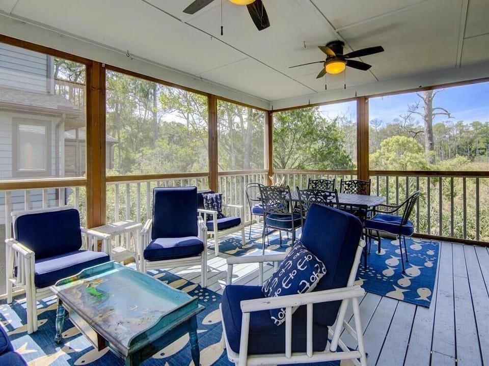 Relax in the cozy screened porch, furnished with comfortable seating and a dining area, offering a peaceful retreat amidst nature.